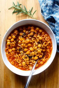 a white bowl filled with pasta and sauce on top of a wooden table next to a blue towel