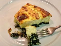 a piece of quiche with spinach and cheese on a plate next to a fork