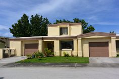 a yellow house with brown garage doors and green grass in front of the house, on a sunny day