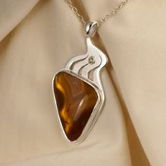 Designed to show off the dramatic bands of the agate, winding silver flows upward to the bail (loop). A very pretty champagne diamond can be traced back to just a hint of quartz crystals in the top of the agate. The agate has been set on a reflective background to show off its transparent, honey-colored stripes as if you were holding it up to a light. The overall effect makes the agate glow. It is set in a heavy bezel with a bright cut around its rim. The agate is 20 x 30 x 4.5 mm. Laguna Agate is a very highly prized for its colored banding. It is found in an area of Mexico that is south of El Paso, Texas. The 0.06 carat diamond is 2.5 mm. The pendant is 50 mm tall by 15 mm wide (about 2 x 1 inches). The sterling silver chain is included. Elegant Brown Necklace With Polished Finish, Elegant Brown Jewelry With Polished Finish, Elegant Brown Polished Jewelry, Elegant Teardrop Agate Necklace, Modern Twist Jewelry With Gemstone For Gift, Elegant Amber Sterling Silver Necklace, Elegant Agate Jewelry For Anniversary, Elegant Brown Sterling Silver Necklace, Elegant Agate Necklace With Large Pendant