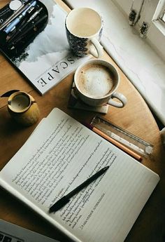 an open notebook sitting on top of a wooden table next to a cup of coffee