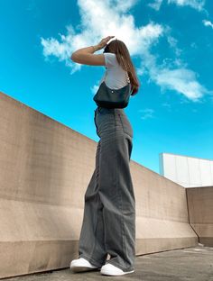 a woman standing in front of a wall with her hand on her head and looking up at the sky