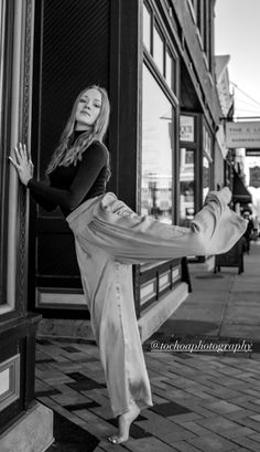 black and white photograph of a woman dancing on the sidewalk in front of a store