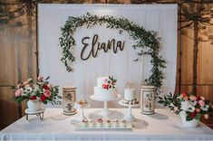 a table topped with cakes and flowers next to a sign that says elana on it