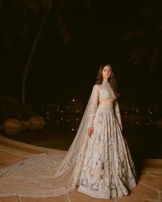 a woman in a wedding dress standing on a patio at night with palm trees behind her