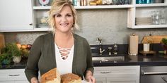 a woman holding a loaf of bread in her hands and smiling at the camera while standing in front of a kitchen counter