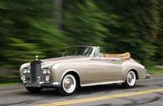 an old car driving down the road with trees in the background