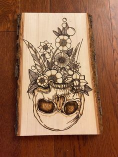 a wooden plaque with a drawing of a human skull and flowers on it's head