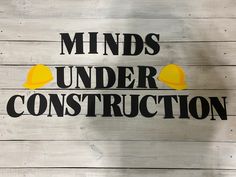 a sign that says minds under construction on the side of a wooden building with yellow hard hats