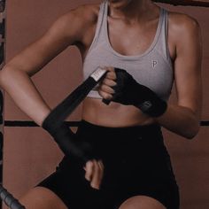 a woman in grey tank top and black shorts holding a boxing glove with both hands