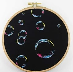 an embroidery project with black background and multicolored circles on the front, hanging from a wooden hoop