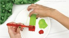 someone is painting a paper plate with green and red paint on it while another hand holds a brush