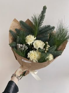 a person holding a bouquet of white flowers and greenery in front of a wall