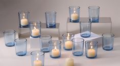 many different types of candles in glass vases on a white table with grey background