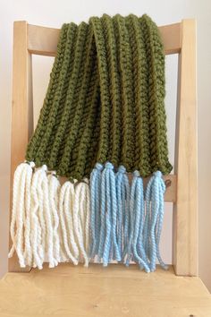 Super cozy and super chunky army green scarf with blue and white contrasting tassels. Made from a blend of acrylic and wool for warmth and comfort.  Hand crocheted in the Bronx.  Content:  Scarf: 77% Acrylic, 20% Wool, 3% Viscose; Tassels: 80% Acrylic, 20% Wool Care: Hand wash, lay flat to dry Merino Wool Scarf, White Scarf, Green Scarf, Super Chunky, Gorgeous Fabrics, Wool Scarf, Green And White, Bronx, Hand Crochet