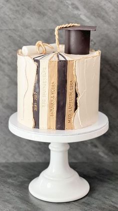 a cake decorated with books and a graduation hat on top of a white pedestal in front of a gray background