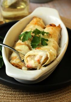 a black plate topped with a white dish filled with lasagna and garnished with cilantro