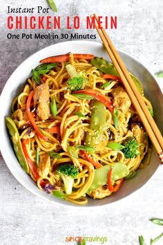 a white bowl filled with noodles, broccoli and carrots next to chopsticks