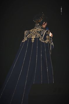 a woman dressed in an elaborately designed blue and gold gown, standing with her hands on her hips