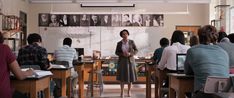 a woman standing in front of a class room full of people with their backs turned to the camera