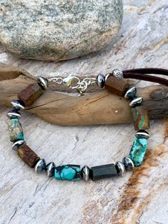 This handsome Turquoise and Leather beaded bracelet is made with  Tubes of rough stock, natural Turquoise in shades of Blues and Browns.  Sterling Navajo Pearl Saucer beads and a Brown Leather Tab capture the Earthy, Rustic, Masculine Look.  One Hilltribe Silver Sun bead is on the leather Tab.  Each  bracelet is unique and handcrafted by me.   Sterling Lobster Clasp and 1 inch Sterling Cable Chain Select your size: Medium: fits a 6.5" to 7" wrist Large: fits a 7" to 7.75" wrist DM me if you would like a differnet size Adjustable Southwestern Bracelets With Natural Stones, Southwestern Style Adjustable Bracelets With Natural Stones, Southwestern Bracelets With Natural Stones And Adjustable Fit, Rustic Adjustable Turquoise Beaded Bracelets, Earthy Turquoise Bracelets For Festival, Rustic Handmade Turquoise Beaded Bracelets, Rustic Turquoise Bracelets For Jewelry Making, Southwestern Natural Stones Beaded Bracelets For Festivals, Southwestern Natural Stone Beaded Bracelets For Festivals