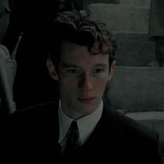 a man in a suit and tie standing next to some stairs with other people behind him