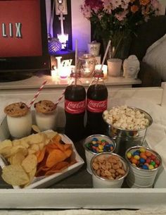 a tray filled with snacks and drinks on top of a bed next to a tv