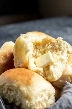 rolls with butter are piled on top of each other in a gray cloth basket, ready to be eaten