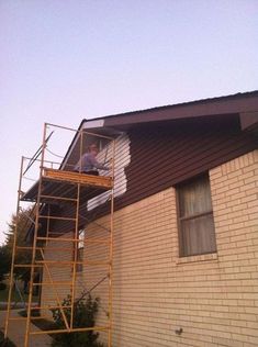 a man standing on a scaffold in front of a house with a ladder