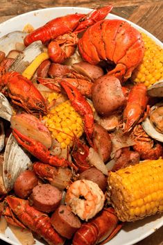 lobsters, corn on the cob and mussels are served in a white bowl