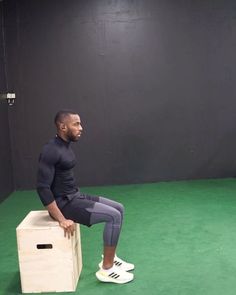 a man sitting on top of a wooden box in a green floored gym area