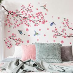 a bed with pink flowers and birds painted on the wall above it, next to a white vase