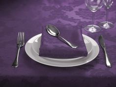 a purple table cloth with silverware and wine glasses on it, next to a white plate