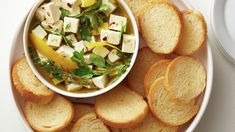 a white bowl filled with bread and soup next to a plate of slices of bread