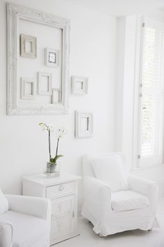 a white living room with two chairs and a table in front of the mirror on the wall