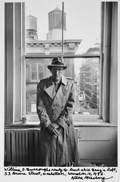 an old photo of a man in trench coat and hat standing next to a window