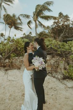 a bride and groom embracing on the beach with palm trees in the backgroud