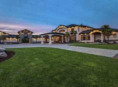 a large house with lots of windows and lights on it's front lawn at dusk