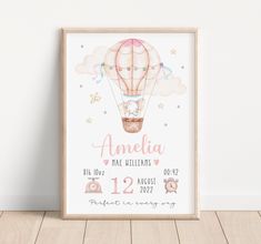 a pink hot air balloon birth print with the name and age on it, in front of a white wall