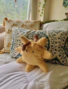 a stuffed animal sitting on top of a bed next to pillows and pillows in front of a window