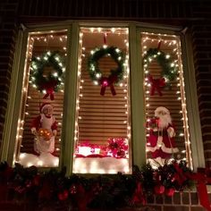 two christmas decorations in the window of a house with lights and wreaths on it