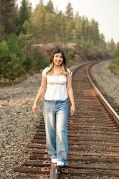 a woman standing on train tracks with trees in the background