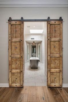 an open door leading to a bathroom with a tub in the middle and wooden floors