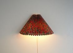 a lamp that is on top of a white wall and has a red shade over it