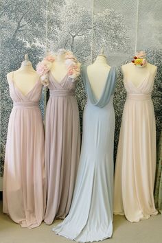 four bridesmaid dresses on mannequins in front of a wall with flowers