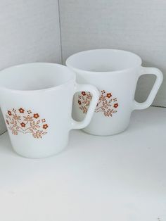 two white mugs sitting next to each other on a counter