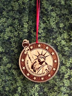 a wooden ornament with the statue of liberty on it's side hanging from a red ribbon