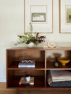 a wooden shelf with books and vases on it in front of two framed pictures