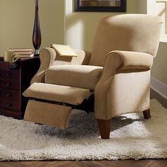 a recliner chair sitting on top of a rug in front of a dresser and lamp