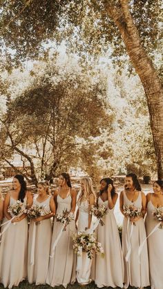 a group of women standing next to each other in front of a tree and holding bouquets